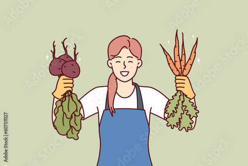 Woman is happy about good harvest of beets and carrots and demonstrates fresh vegetables with useful vitamins and minerals. Girl seller of farmer fair smiles offering to buy delicious vegetables