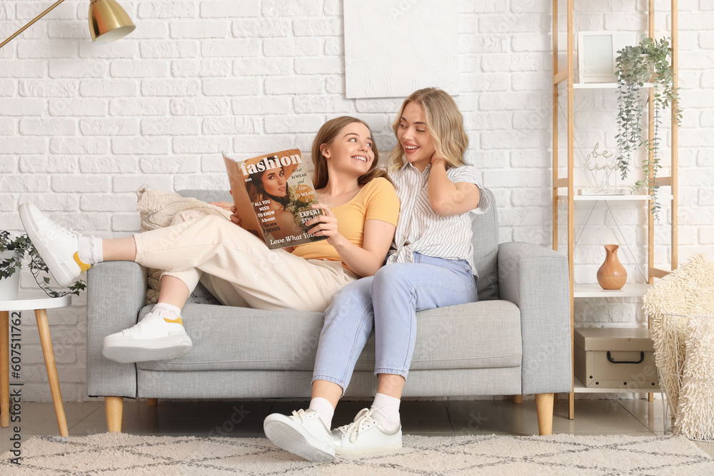 Young sisters reading magazine on sofa at home Young sisters reading magazine on sofa at home