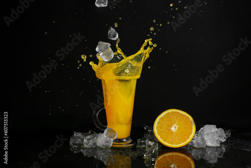 Glass of fresh orange juice with splashes and ice on dark background