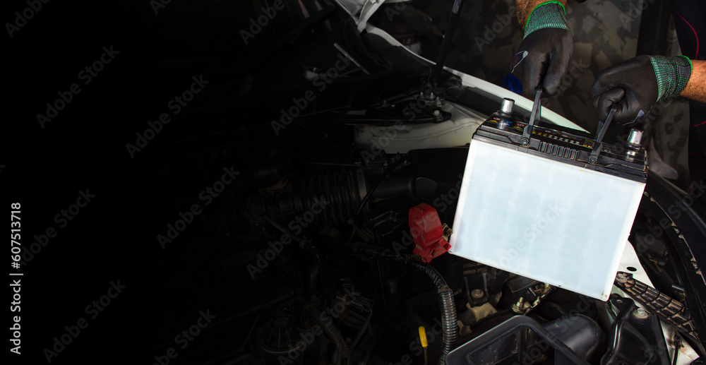 Auto mechanic is pulling up an car old battery for replacement, copy space on black background, car maintenance service concept. Auto mechanic is pulling up an car old battery for replacement, copy space on black background, car maintenance service concept.