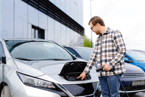 Young man plugging charging cable into the car socket. Electric car charging concept