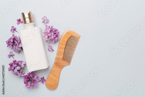 Shampoo with flowers and comb on color background  top view