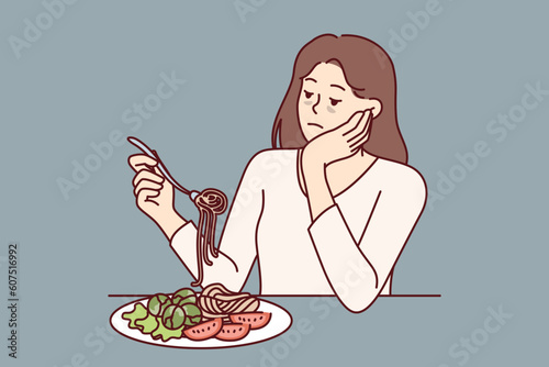 Woman suffering from anorexia is sad due to lack of appetite and sits at table with spaghetti and salad in plate. Skinny girl with sickly appearance suffers from anorexia after wrong diet