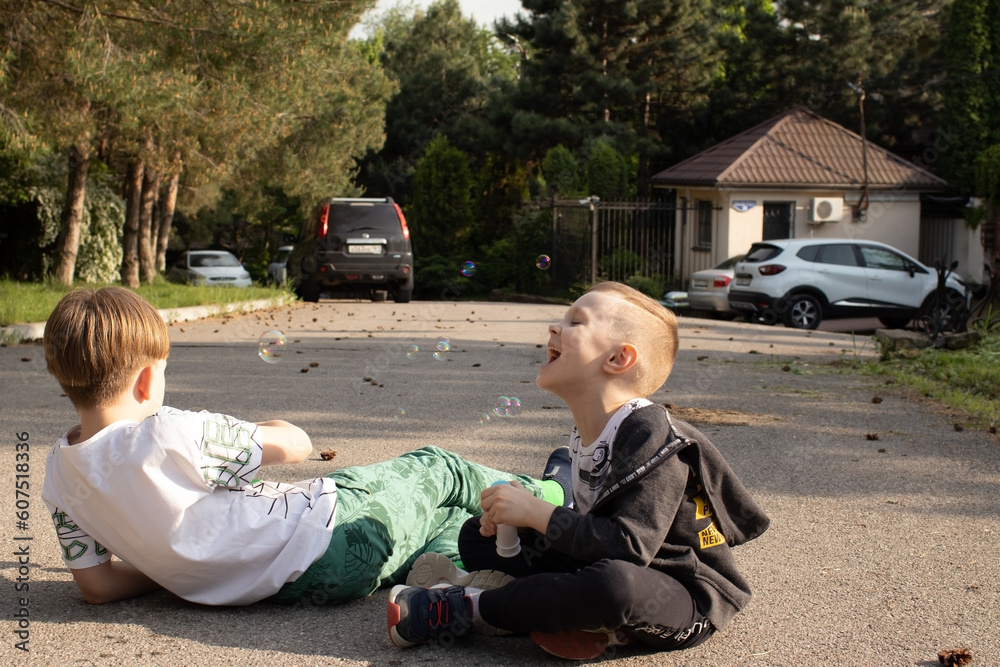 two brothers blow bubbles while sitting on the road by the backyard on a summer holiday two brothers blow bubbles while sitting on the road by the backyard on a summer holiday