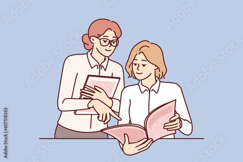 Women read magazine and discuss fashion trends or article by journalist with city news. Girl employee of store or cafe demonstrates to visitor magazine-catalog of products or restaurant menu