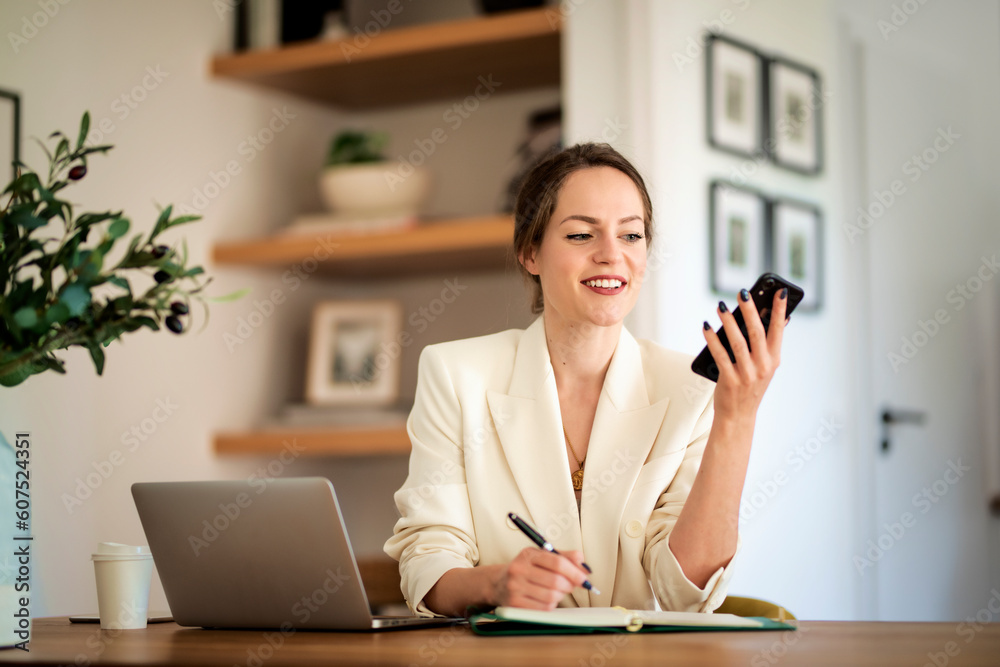Young businesswoman using mobile phone in front of laptop and working from home Young businesswoman using mobile phone in front of laptop and working from home