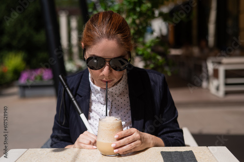Blind woman in business suit drinking ice coffee in outdoor cafe. 