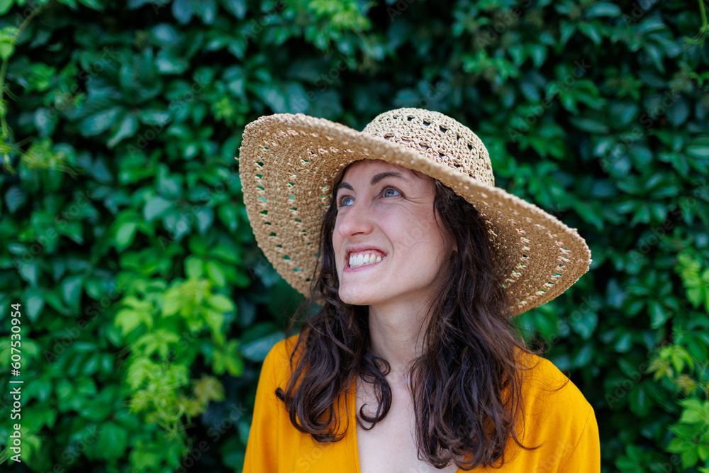 portrait of a young happy brunette in a straw hat. The girl smiles and enjoys her vacation outdoors.