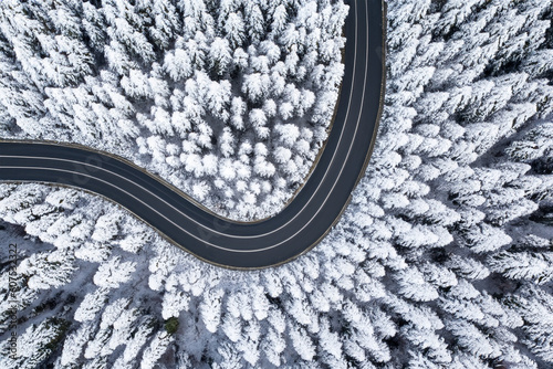 Road in snow covered forest, top down aerial view. Top aerial view of snow mountain landscape with trees and road. © kanpisut