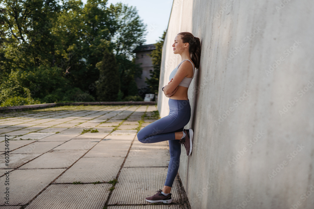 Side view of young sporty woman in sportswear excercising in front of concrete wall in the city. Side view of young sporty woman in sportswear excercising in front of concrete wall in the city.