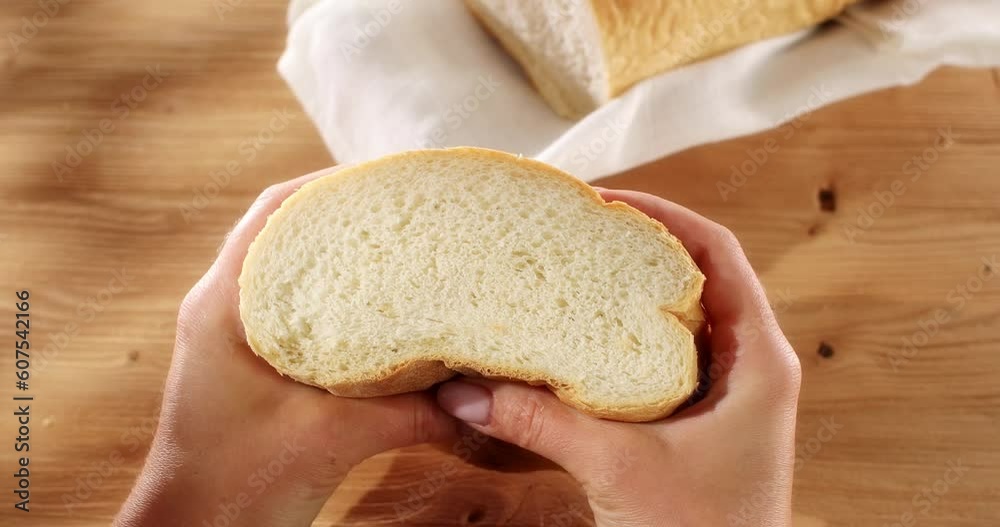 Female hands squeeze fresh bread. Check bread freshness. Wooden background. Slow mation. Sunny day. First person view. 