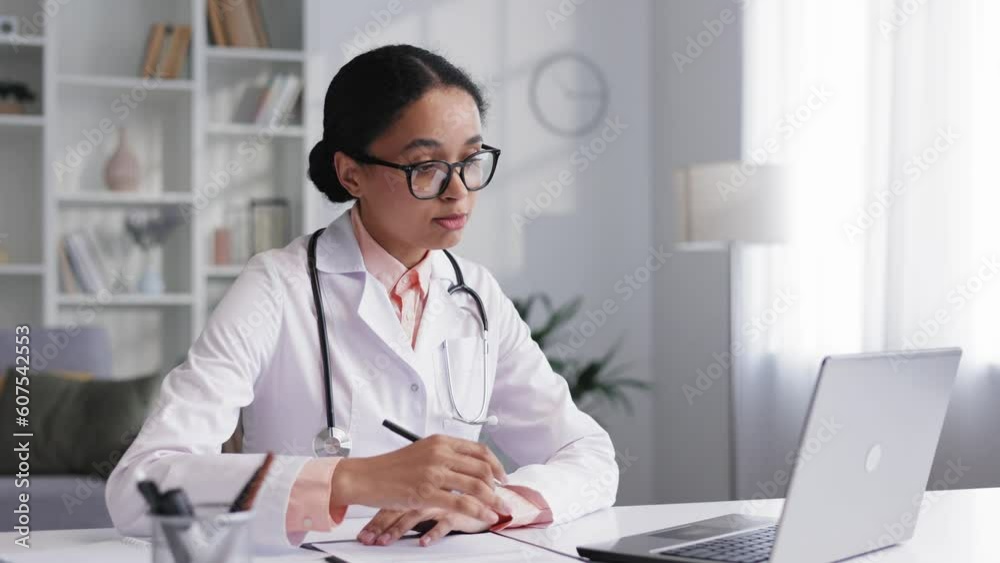 Attractive young African American female doctor wearing glasses is making an online video call consulting a patient on a laptop. Video conference paramedic therapist. Telemedicine pandemic concept. Attractive young African American female doctor wearing glasses is making an online video call consulting a patient on a laptop. Video conference paramedic therapist. Telemedicine pandemic concept.