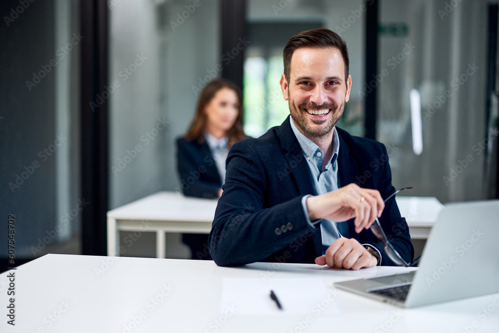 Portrait of a smiling businessman working over a laptop and holding his glasses. Portrait of a smiling businessman working over a laptop and holding his glasses.