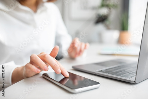 Young caucasian businesswoman using smartphone with blank screen at table with laptop in office, selective focus