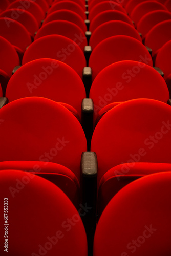 Algumas fileiras de poltronas na cor vermelha em um teatro vazio.