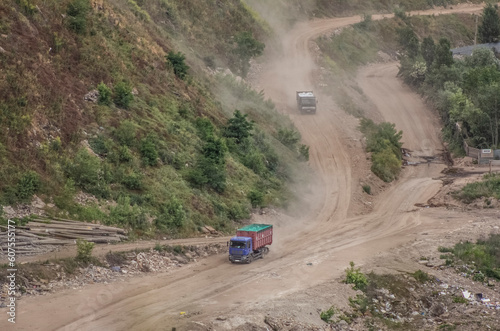 Technical industrial landscape, garbage trucks drive along a dusty road inside a quarry, leaving plumes of dust and transporting construction waste for disposal