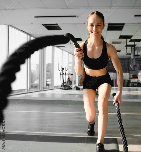 Athletic Female in a Gym Exercises with Battle Ropes During Her Fitness Workout High-Intensity Interval Training. She's Muscular and Sweaty photo