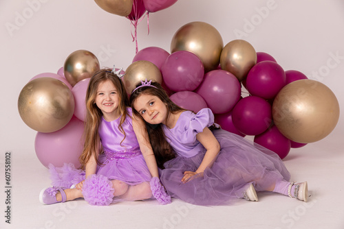 Birthday celebration concept, little princess in lilac dresses, cheerful preschool girl party, two cute girls sitting with balloons on the background, copy space