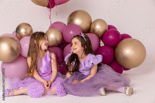 Happy birthday celebration concept, little princess in lilac dresses, cheerful preschool girl party, two happy girls sitting with balloons on the background, copy space