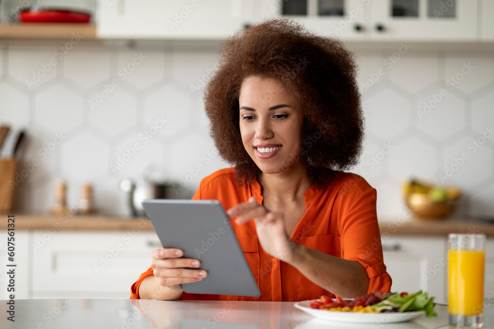 Young Smiling Black Woman Using Digital Tablet During Breakfast In Kitchen Young Smiling Black Woman Using Digital Tablet During Breakfast In Kitchen