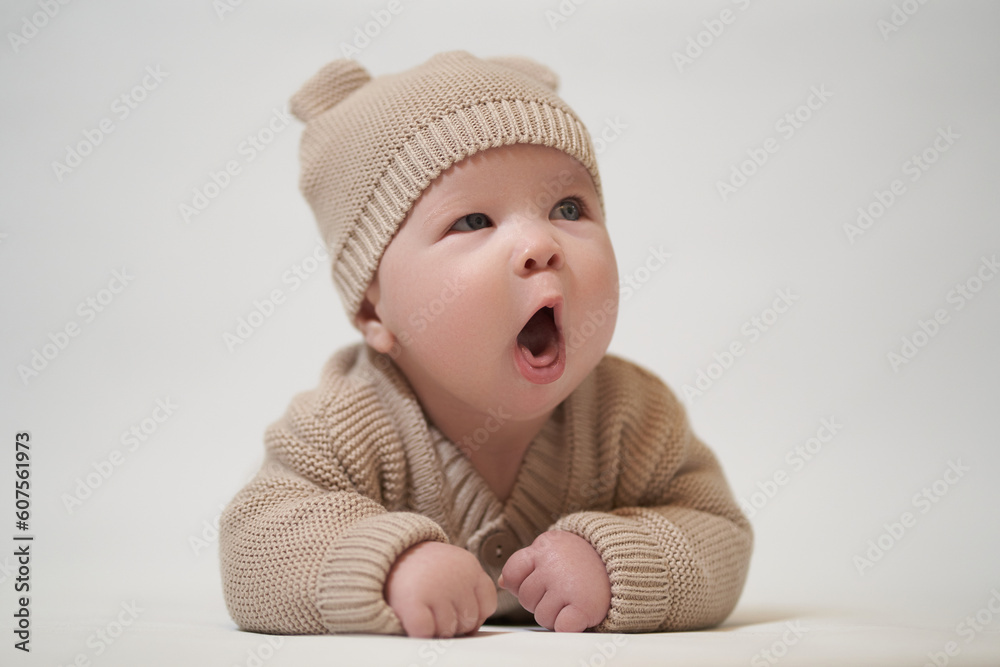 Newborn baby yawns lying on his stomach in knitted clothes on a white background Newborn baby yawns lying on his stomach in knitted clothes on a white background