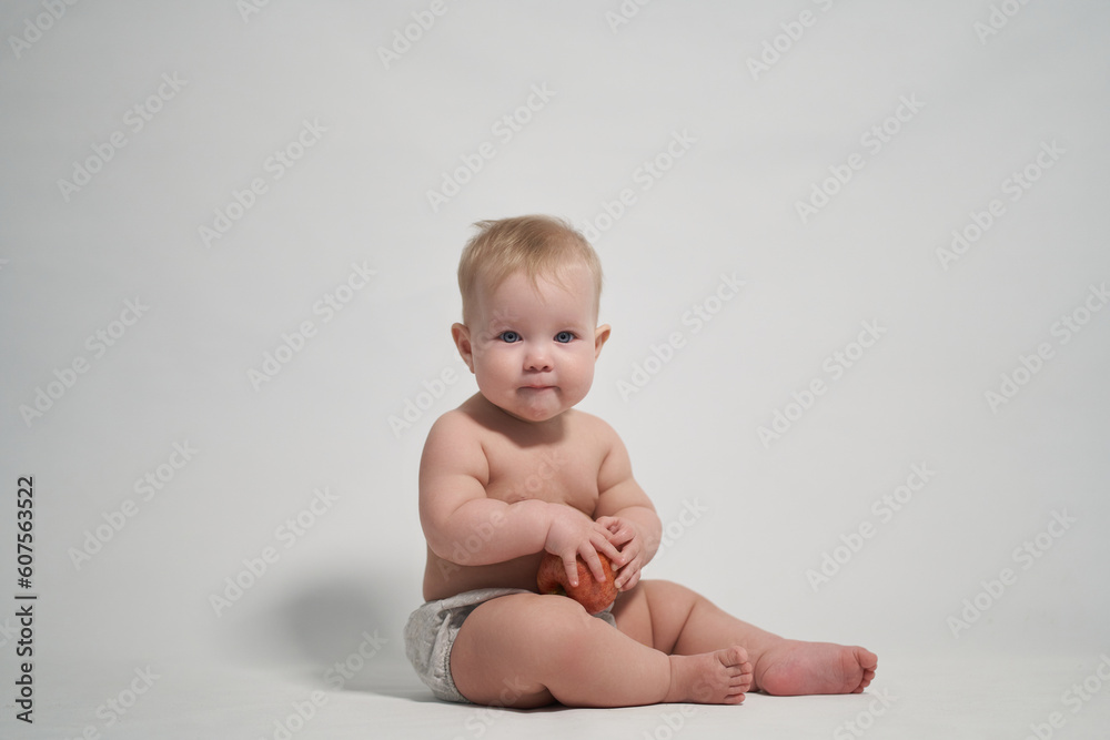 a child of 7 months sitting on the pope holds a red apple in his hands. photography on a light background a child of 7 months sitting on the pope holds a red apple in his hands. photography on a light background