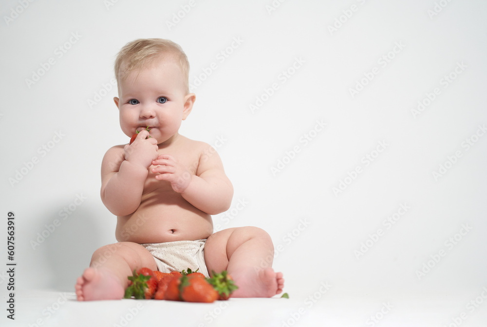 A six-month-old baby eats red strawberries, takes pictures on a light background A six-month-old baby eats red strawberries, takes pictures on a light background