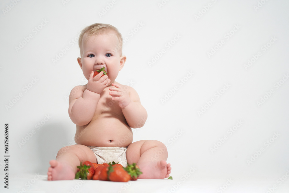 A six-month-old baby eats red strawberries, takes pictures on a light background A six-month-old baby eats red strawberries, takes pictures on a light background