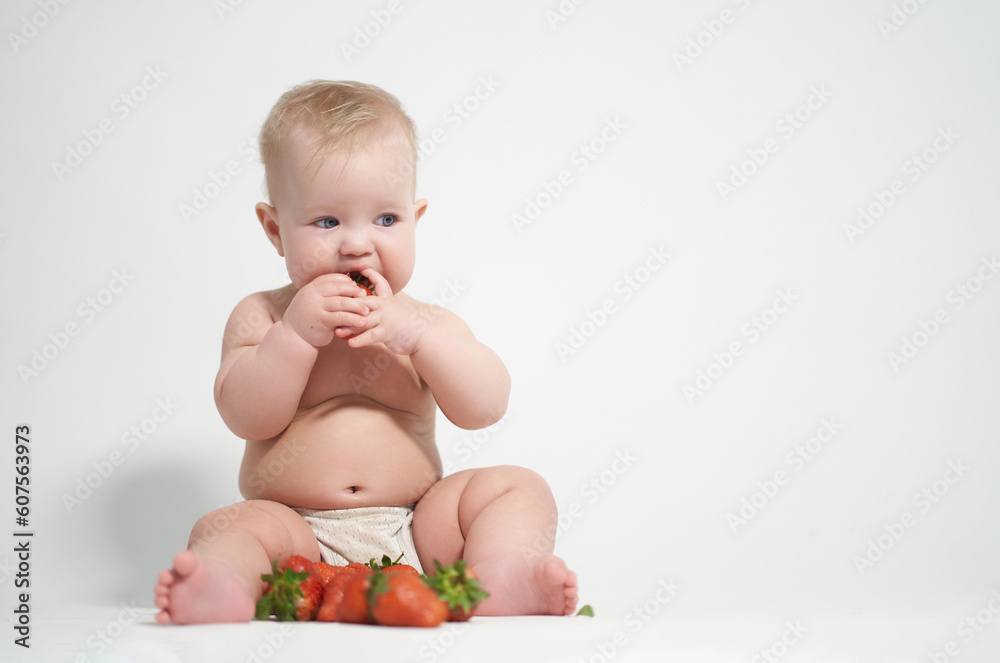 A six-month-old baby eats red strawberries, takes pictures on a light background A six-month-old baby eats red strawberries, takes pictures on a light background
