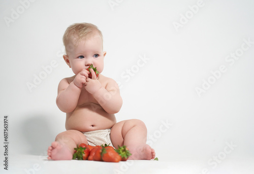 A six-month-old baby eats red strawberries, takes pictures on a light background