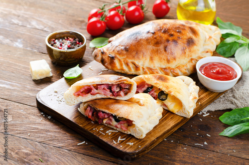 Delicious Pizza Calzone, Italian Pizza Stuffed with Ham and Cheese with Tomatoes and Fresh Basil on Wooden Background