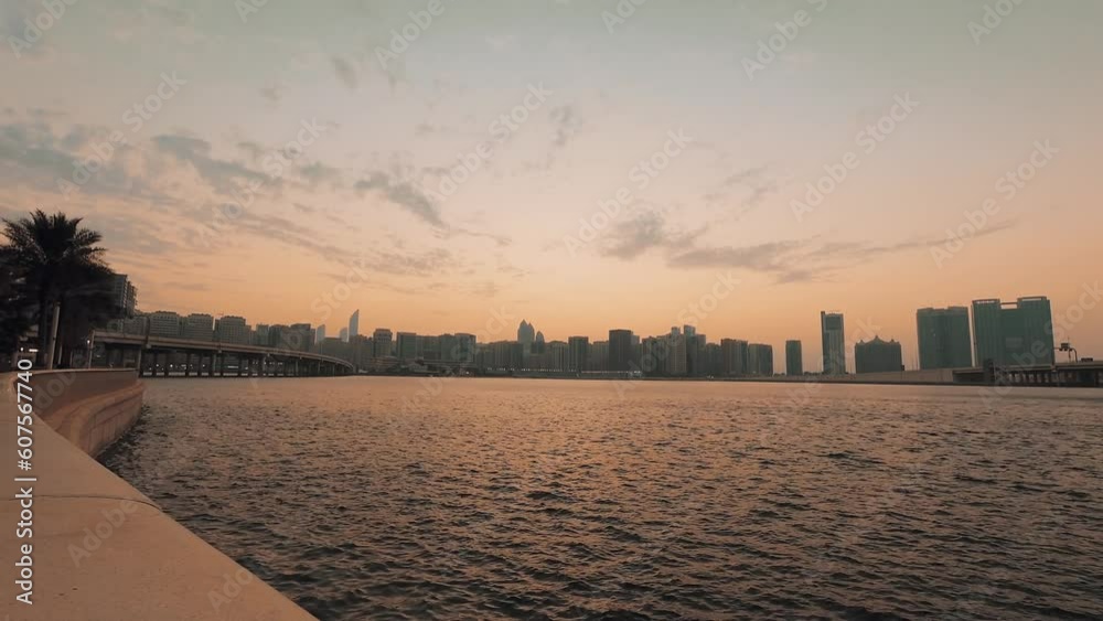 Zoom out Abu Dhabi city skyline on sunset time with water ripples timelapse from the breakwater near mall. Few clouds on orange sky hot evening Zoom out Abu Dhabi city skyline on sunset time with water ripples timelapse from the breakwater near mall. Few clouds on orange sky hot evening
