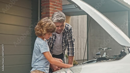 Family members communication. Adult man and boy standing outside and fixing car demages on background of backyard. Teamwork of son and dad for repairing vechical engine. Happy parenthood concept photo