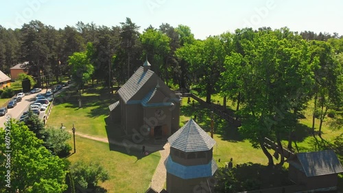 Aerial view Young lithuanians relax on sunday mass by St. Joseph Church in Paluse, Lithuania. Stave Churches in Europe. Old heritage sites. Walls formed by vertical wooden boards. photo