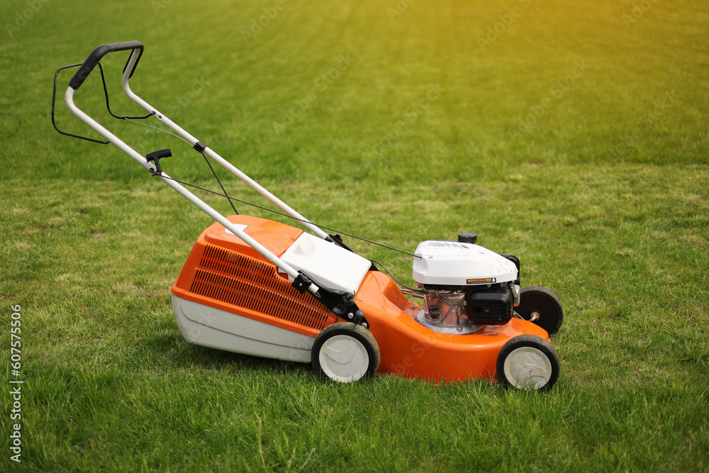 Top view of modern orange-grey electric lawn mower cutting bright lush green grass. Gardening work tools. Rotary lawn mower machine on lawn. Professional lawn care service. Place for text. Top view of modern orange-grey electric lawn mower cutting bright lush green grass. Gardening work tools. Rotary lawn mower machine on lawn. Professional lawn care service. Place for text.