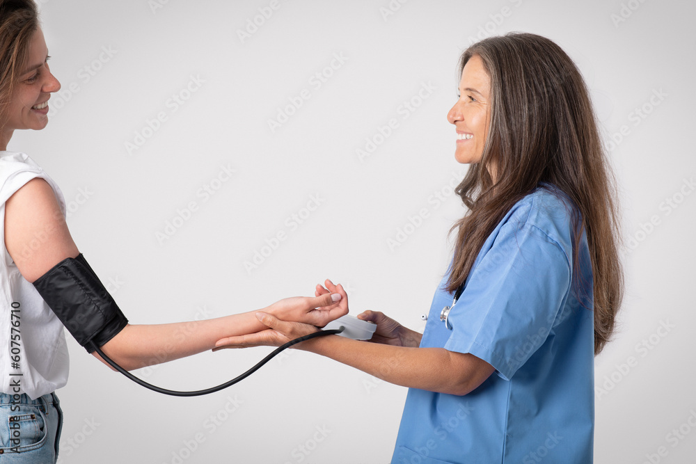 Healthcare, hospital and medicine concept. Cheerful senior doctor woman measuring blood pressure to her lady patient Healthcare, hospital and medicine concept. Cheerful senior doctor woman measuring blood pressure to her lady patient