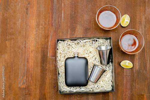 Stainless black metal steel pocket flask, gift box hiking man's set for alcohol with glasses. glasses of whiskey, cognac drink on wooden table background, top view,copy space,mock up, flatlay photo