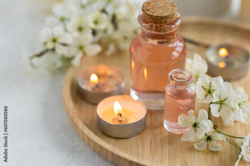 Spa products, aromatherapy, atmosphere of relax. Candles and spa essentials on bamboo tray in bathroom, essential oil, bath salt, towel, sea stone, spring apple tree blooming flowers
