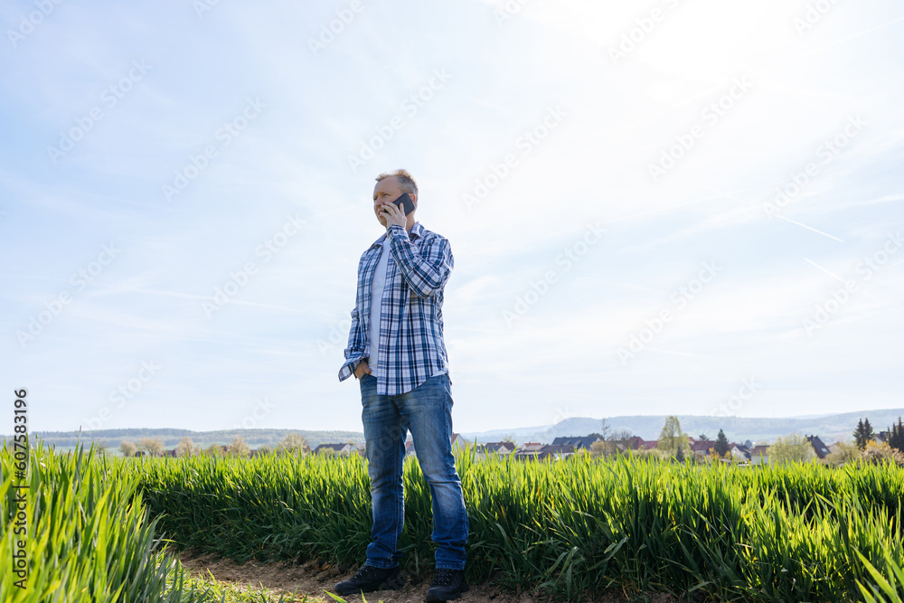 A male farmer stands in a field and talks on the phone. Modern technologies in agriculture