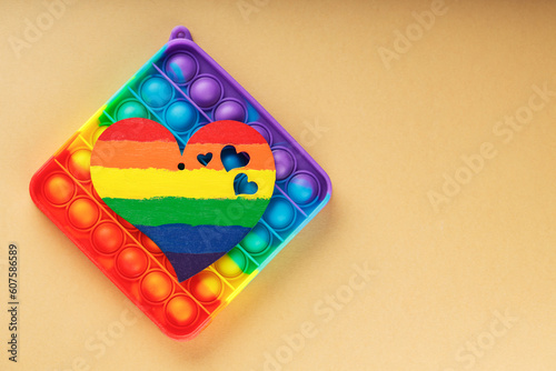 Multicolored pop it fidget toys and rainbow heart on beige background. LGBT equal rights movement and gender equality concept. Top view. Copy space