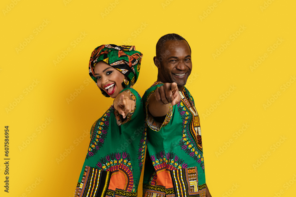 Cute black couple in african costumes pointing at camera