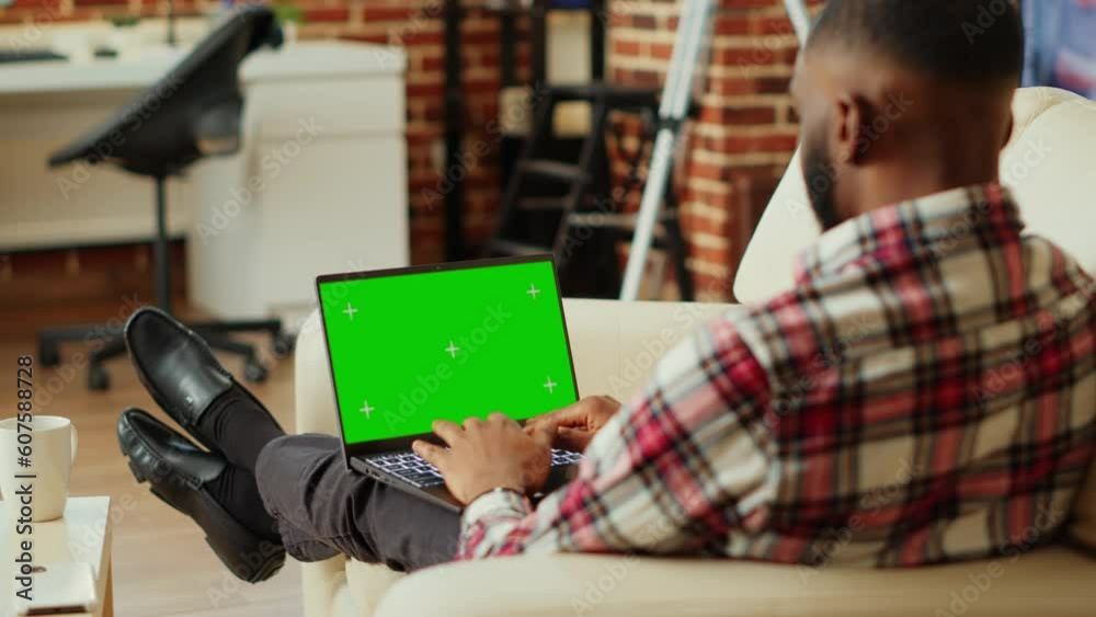 Focused teleworker remotely solving company tasks in stylish apartment personal office, typing data on chroma key mock up laptop green screen. Professional executive working from home