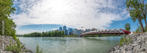 Panoramic skyline view of Calgary, Alberta with Peace Bridge in view over the Bow River in summer spring time on blue sky day with partial clouds. 
