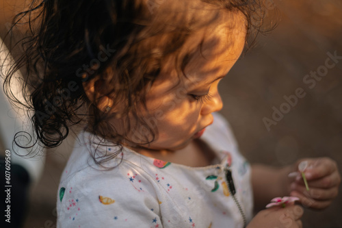 Niña pequeña jugando en un carro mientras observa una flor los rayos del sol se reflejan en su rostro 