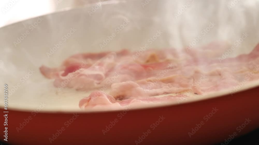 fried bacon.Bacon strips fry in an orange frying pan. keto diet ingredient.appetizing Bacon close-up frying and smoking in a frying pan. 4k footage