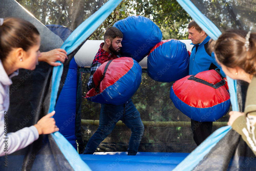 Obraz premium Happy male friends fighting by big stuffed boxing gloves at outdoor amusement playground
