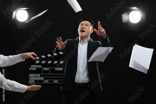 Emotional asian actor performing role while second assistant camera holding clapperboard on stage. Film industry photo