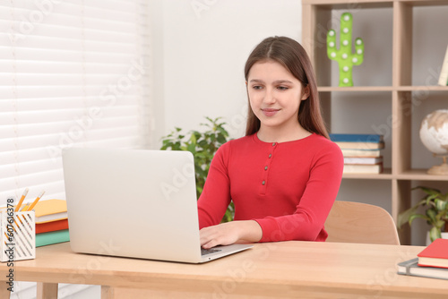 Cute girl using laptop at desk in room. Home workplace