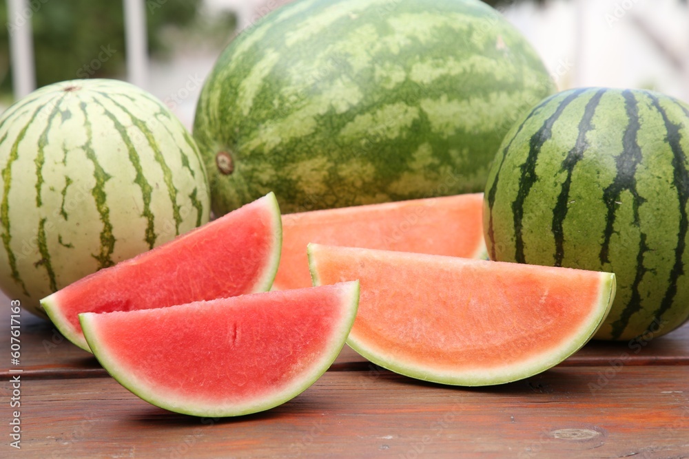 Different cut and whole ripe watermelons on wooden table outdoors Different cut and whole ripe watermelons on wooden table outdoors