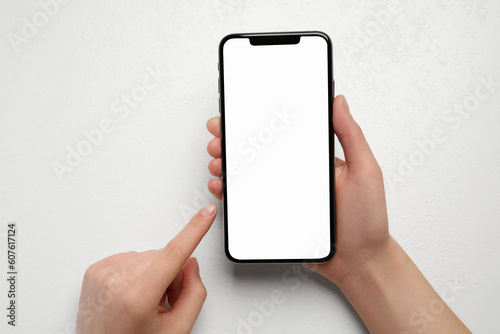 Woman holding smartphone with blank screen at white table, top view. Mockup for design